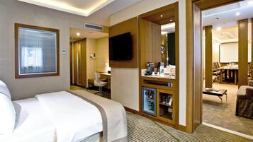 A hotel room with a bed, a desk, a television, and a minibar.