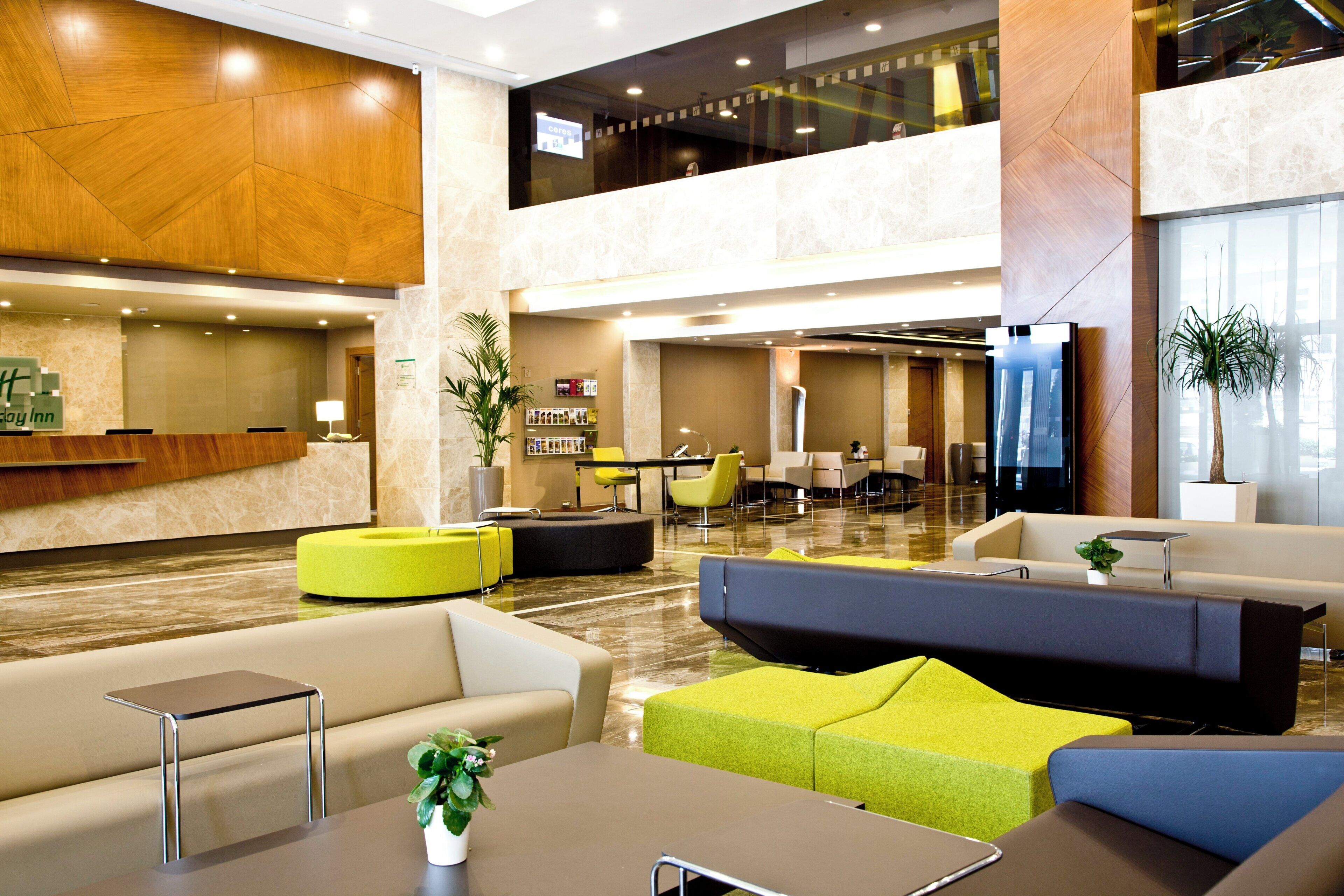 A modern hotel lobby with a reception desk, seating areas, and a staircase.