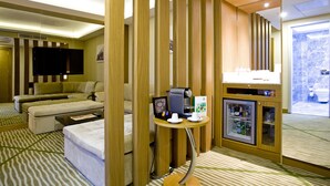 A hotel room with a sofa, a coffee machine, a mini-fridge, and a television. - Holiday Inn Gaziantep - Sehitkamil by IHG (Gaziantep)