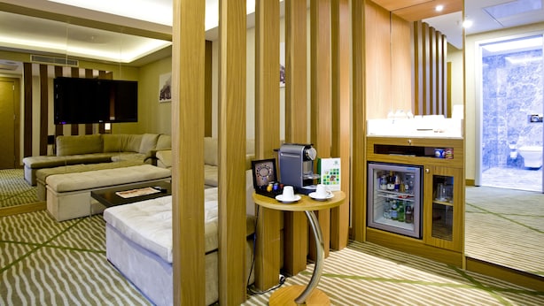 A hotel room with a sofa, a coffee machine, a mini-fridge, and a television. - Holiday Inn Gaziantep - Sehitkamil by IHG (Gaziantep)