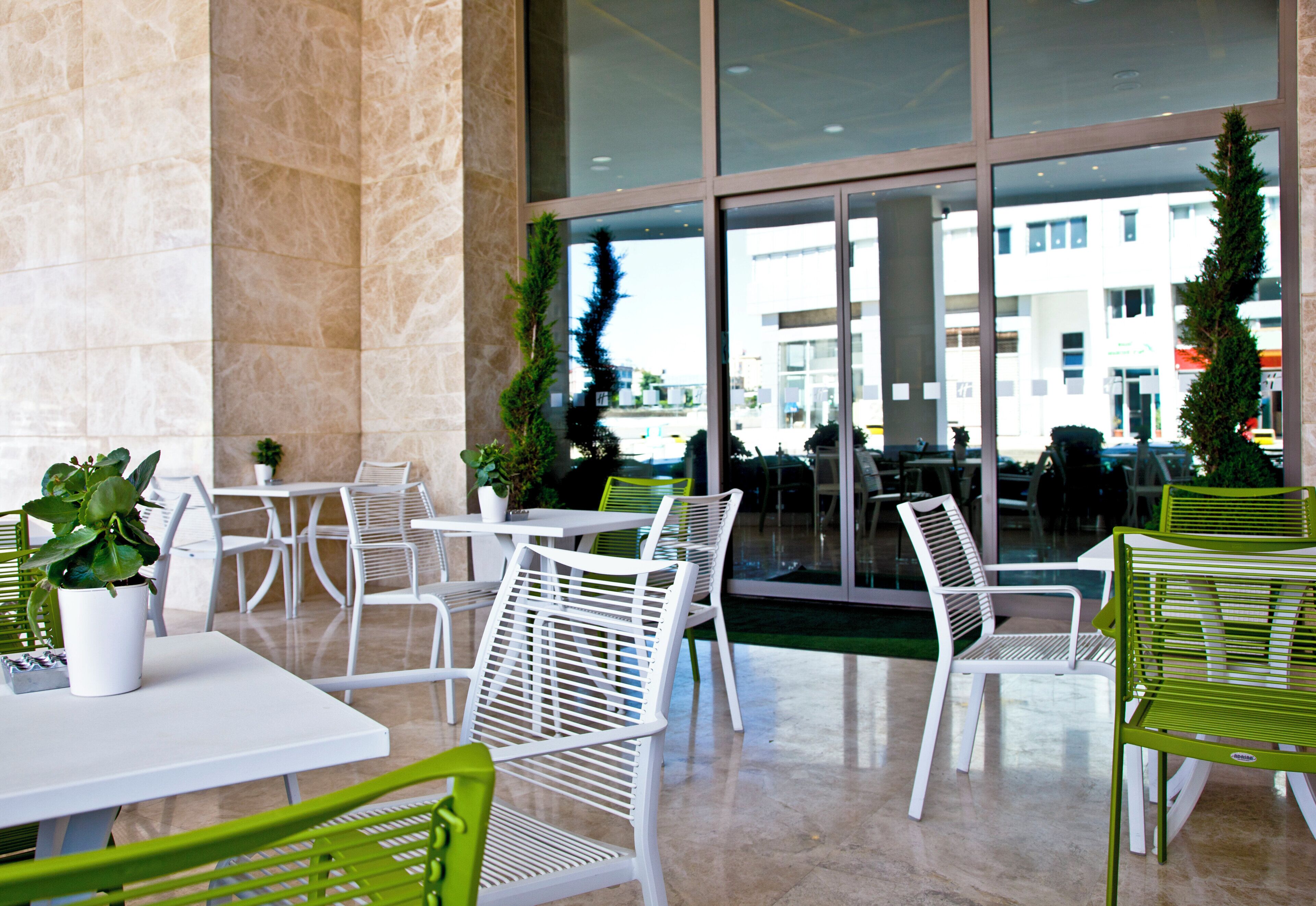Un espace extérieur aménagé avec des chaises, des tables et des plantes en pot, le tout dans des tons de blanc et de vert.