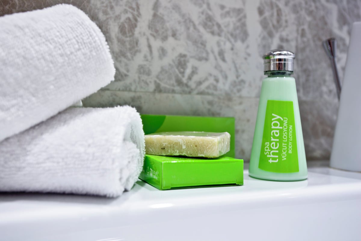 Une salle de bain avec une serviette blanche, un savon vert et une bouteille de lotion pour le corps aux propriétés thérapeutiques, également verte.