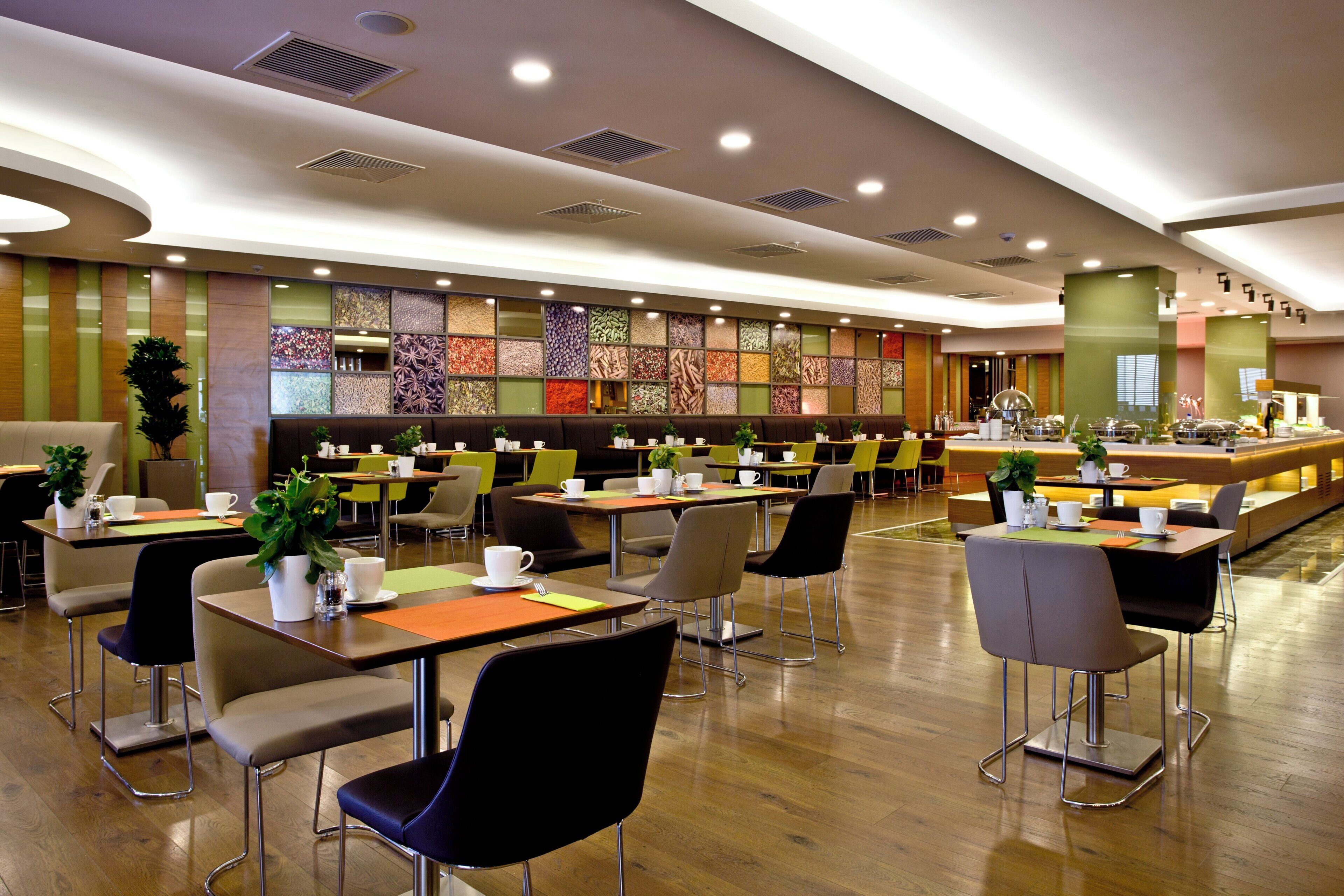 A modern cafe with multiple tables and chairs, a decorative wall with patterned tiles, and a counter with food and drink items.