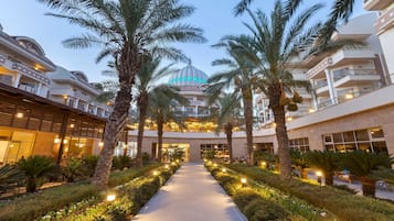 A hotel with a central dome, palm trees, and a well-lit pathway.