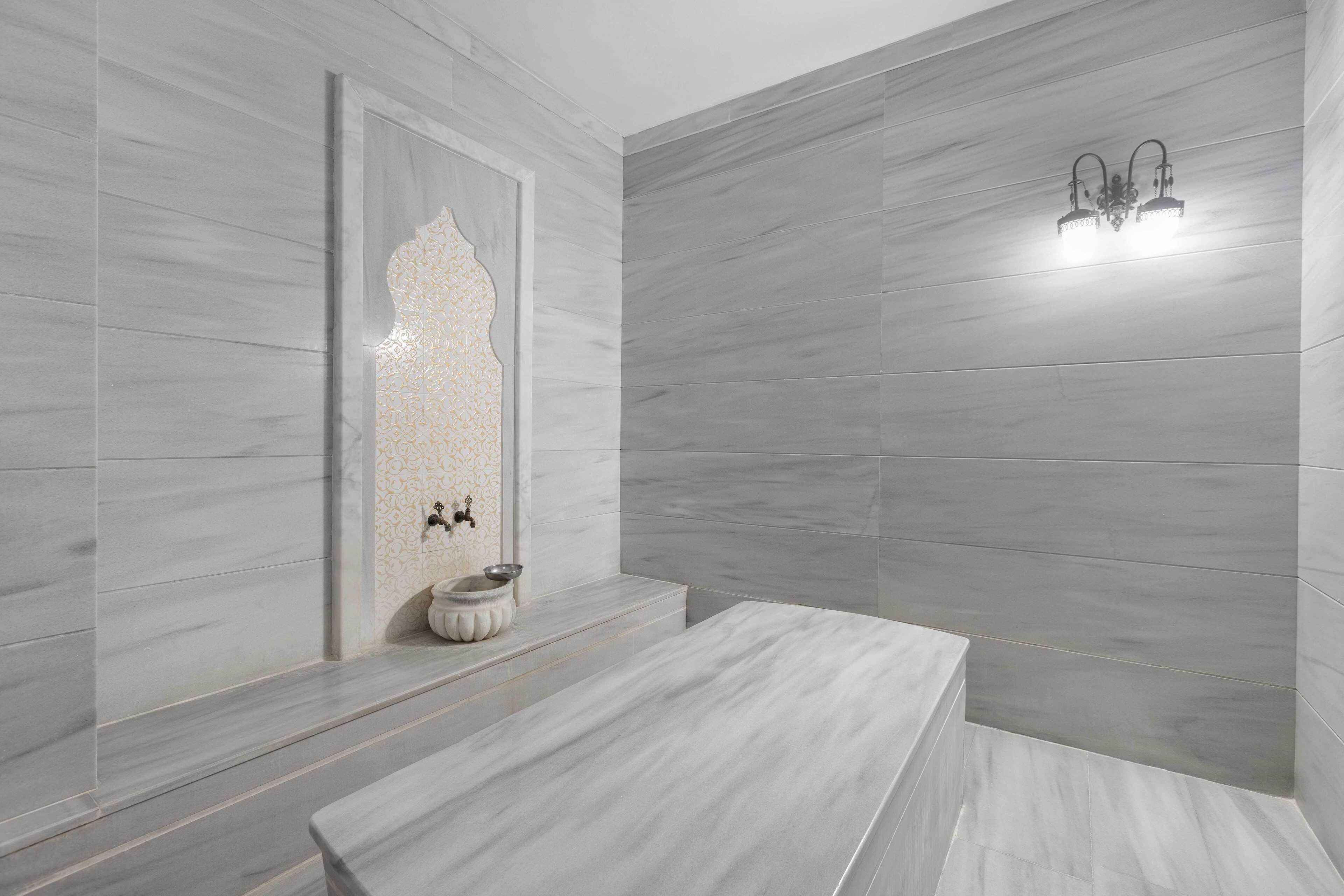 Une salle de bain moderne avec des carreaux de marbre gris, un panneau mural décoratif, un lavabo en forme de vasque et un luminaire fixé au mur.