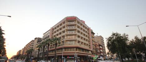 Un hotel de varios pisos con una ubicación destacada en una esquina, que cuenta con balcones y diversas tiendas a nivel de calle.