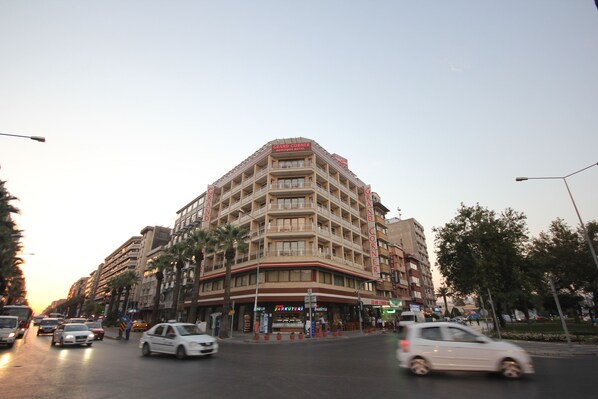 Un hôtel à plusieurs étages, situé dans un emplacement privilégié à l’angle d’une rue, doté de balcons et offrant une variété de boutiques au rez-de-chaussée.