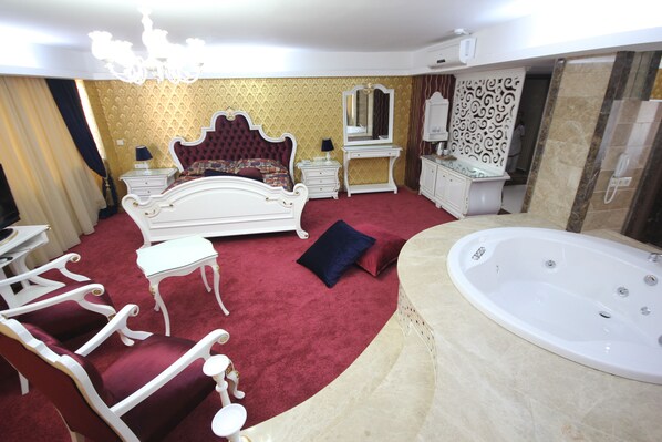 A luxurious bedroom with a large bed, a sitting area with a chair and table, a vanity with a mirror, and a bathtub. - Grand Corner Hotel - Boutique Class (Izmir)