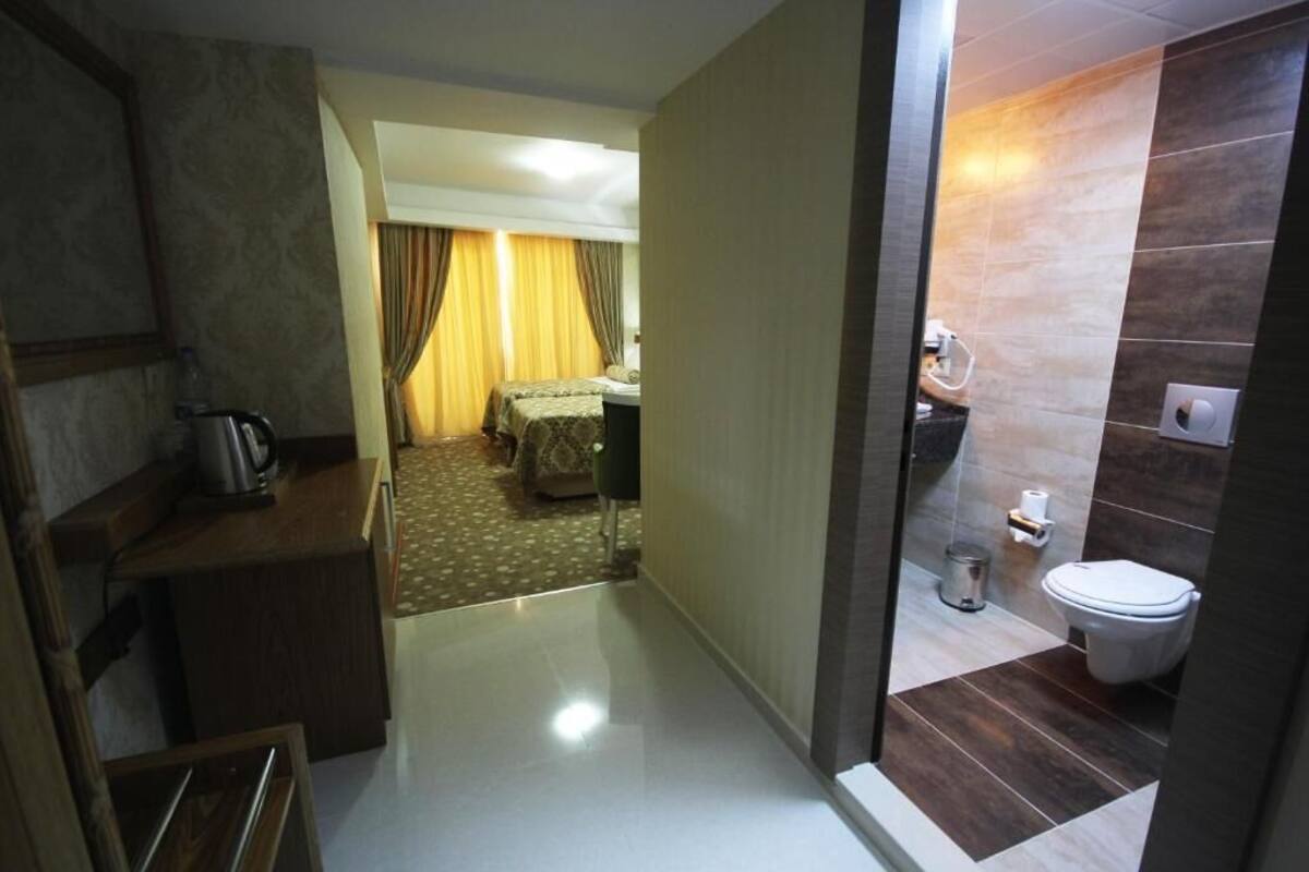 A hotel room with a kitchenette, a bed, a bathroom with a toilet and sink, and a hallway leading to another room.