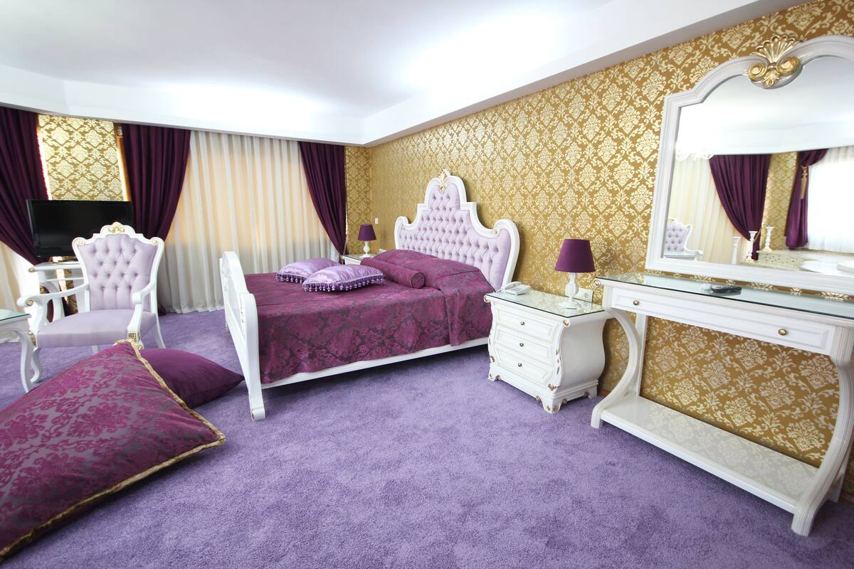 A bedroom with a large bed, a vanity with a mirror, a chair, and a dresser.