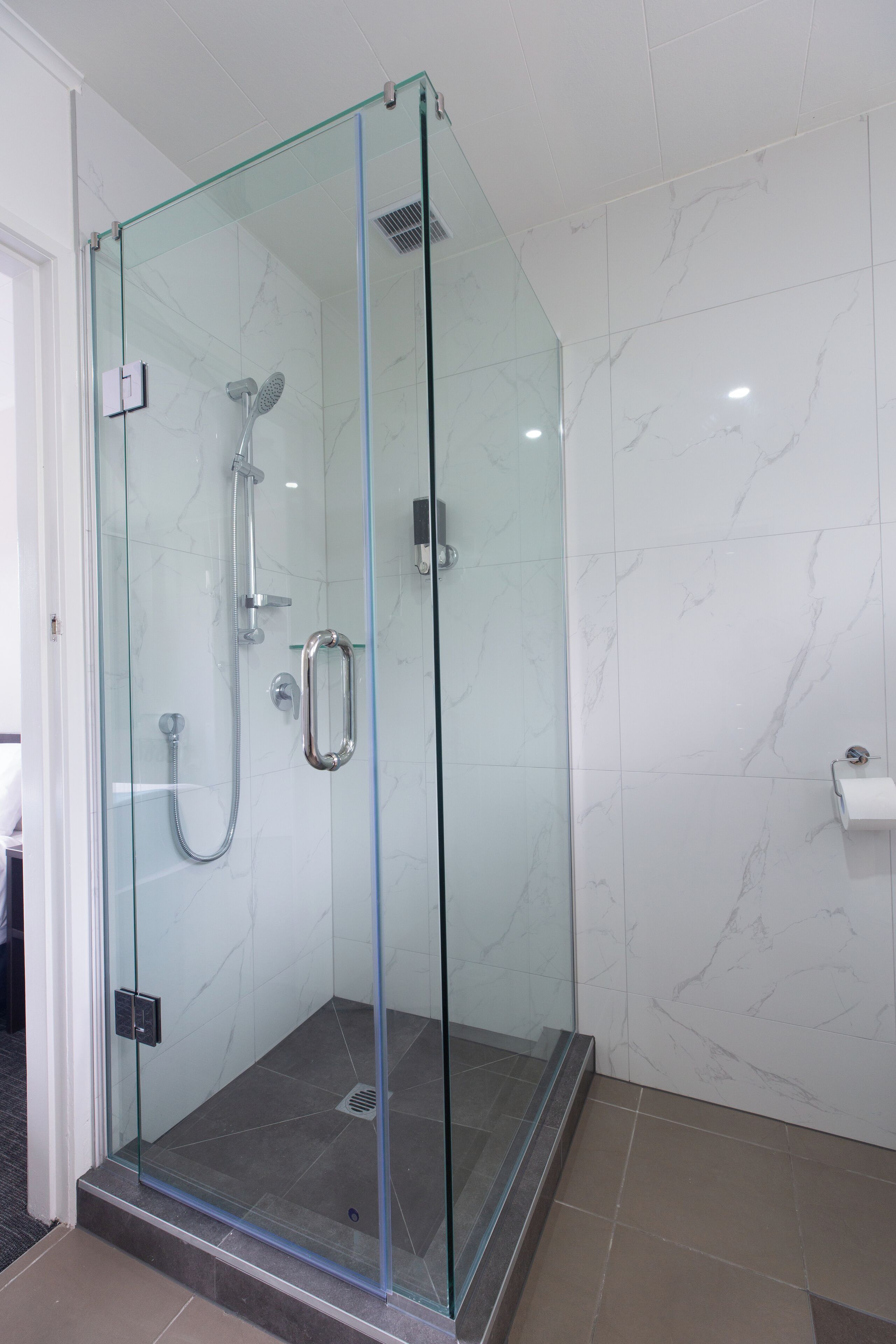 Une douche fermée par des parois en verre, dotée d’un pommeau de douche à main et d’un robinet mural.