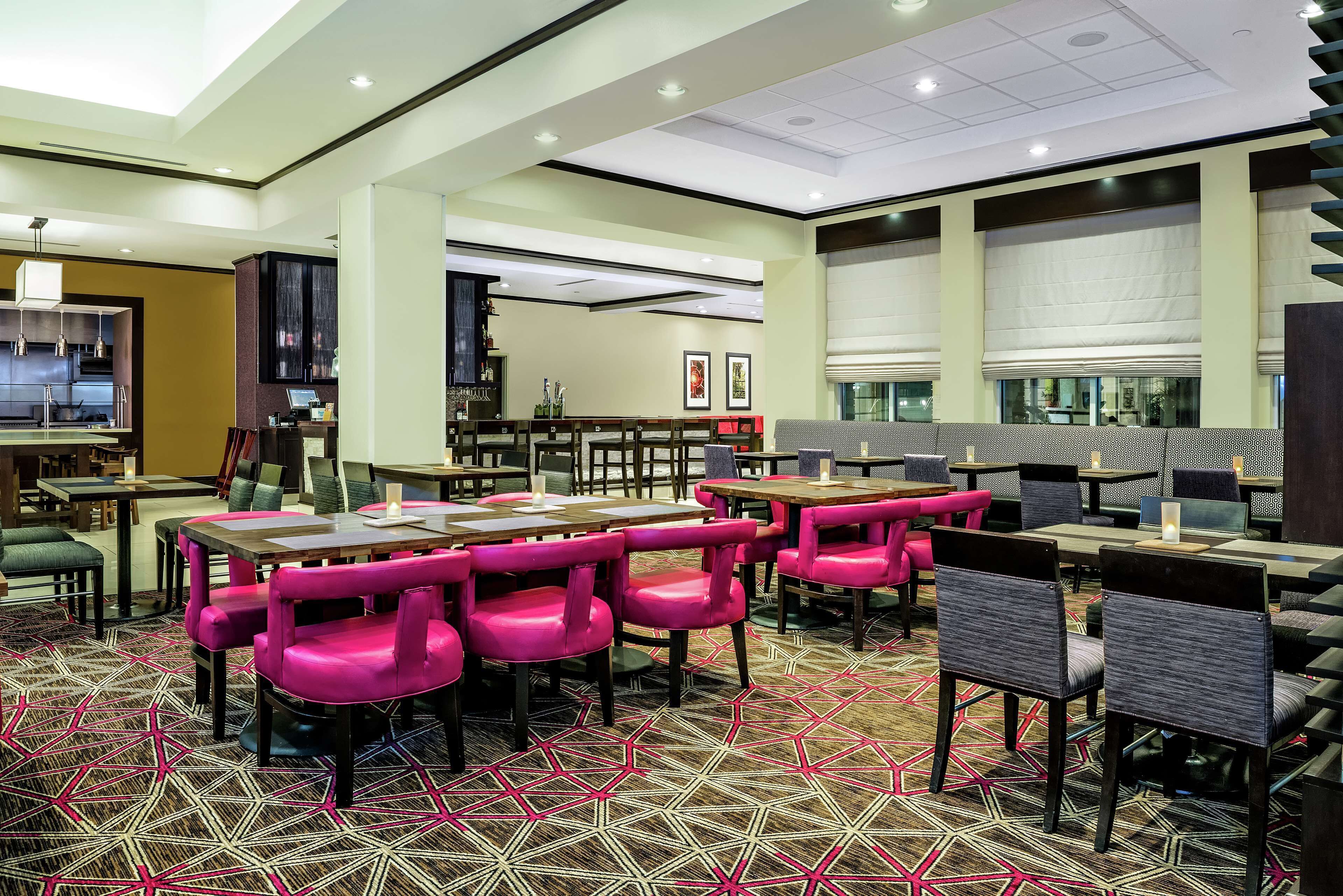 A modern dining area with tables and chairs, a patterned carpet, and a kitchen in the background.