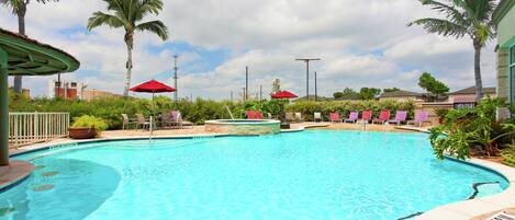 Une piscine entourée de palmiers et de verdure, avec des chaises longues et des parasols.