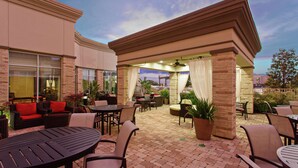 An outdoor patio area with brick flooring, tables, chairs, and potted plants. - Hilton Garden Inn Victoria (Victoria)