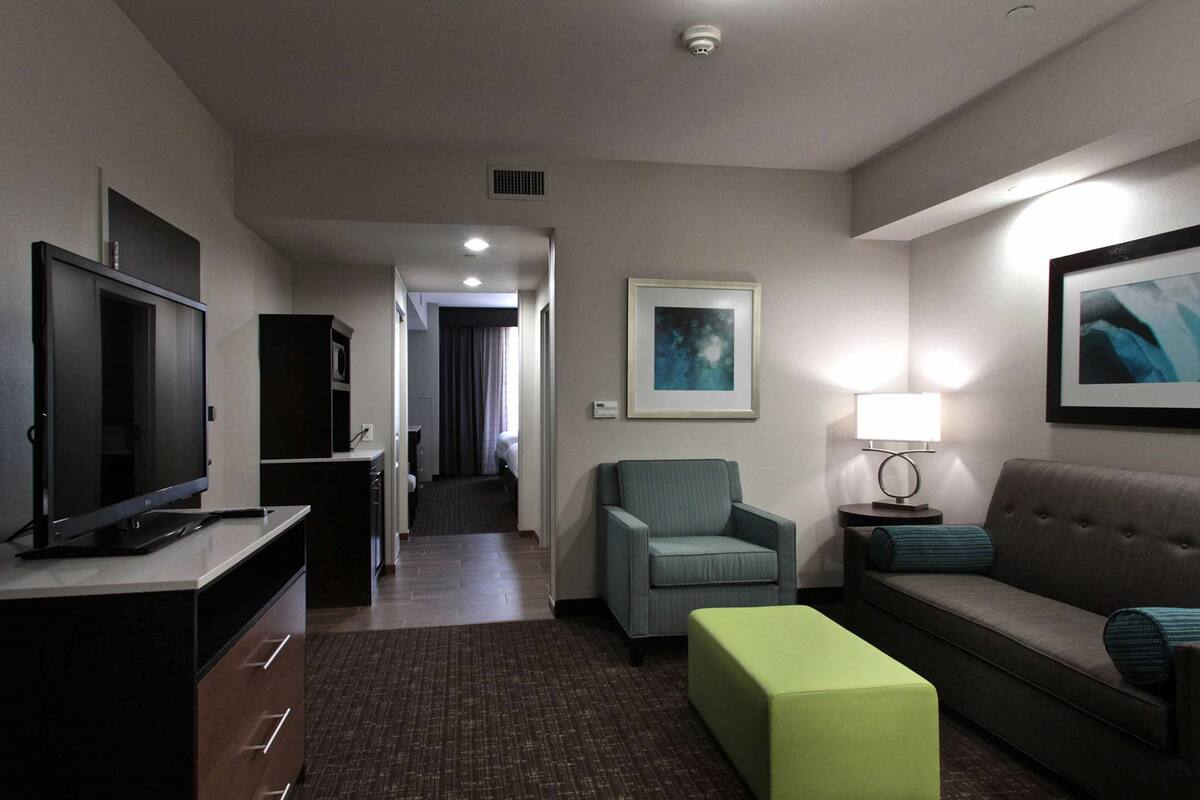 A hotel room with a television, a sofa, a chair, a small table with a lamp, and a framed picture on the wall.