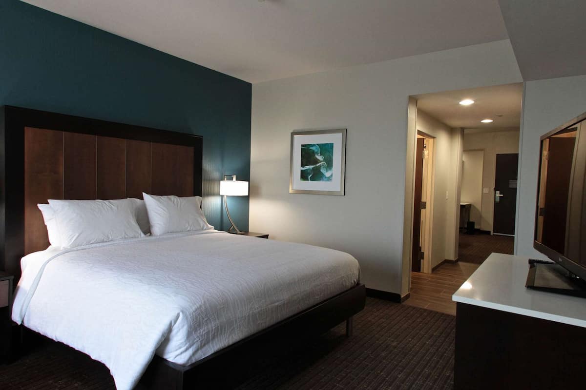 A hotel room with a large bed, a desk, a chair, a lamp, and a framed picture on the wall.