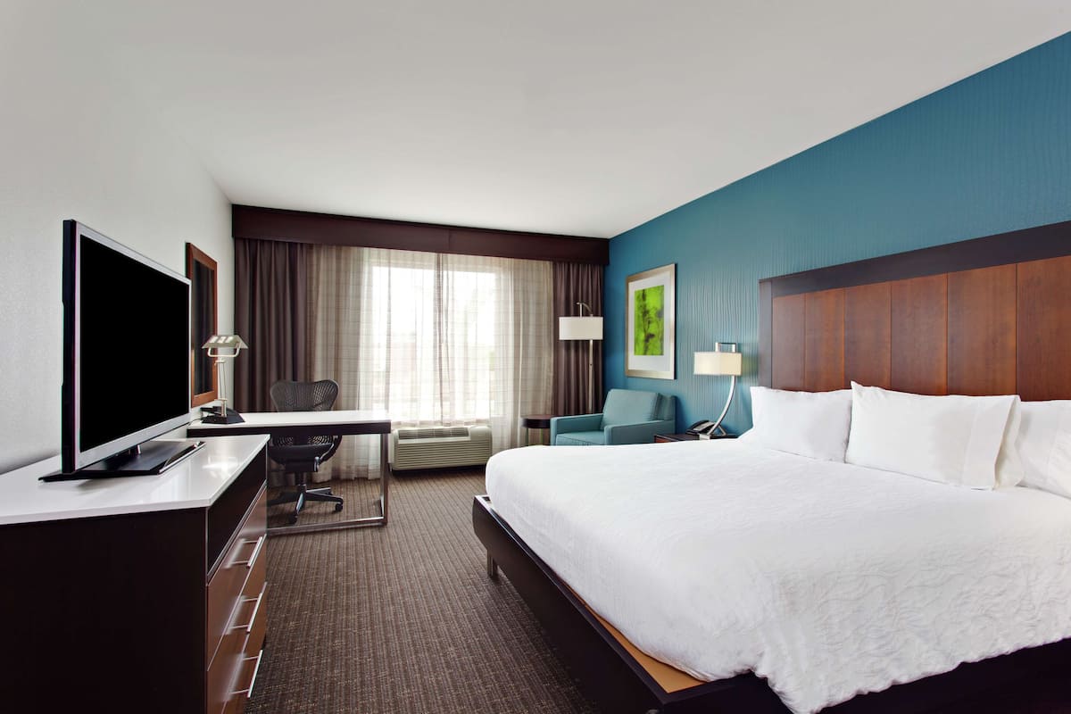 A hotel room with a large bed, a desk with a computer, a TV, and a chair.