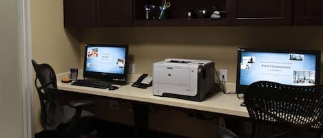 A workspace with two desktop computers, a printer, and office chairs.