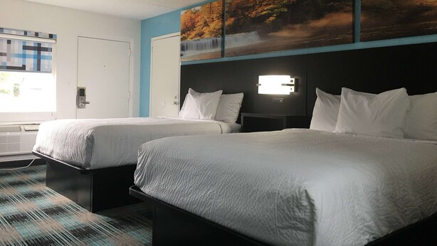 A hotel room with two beds, a window with blinds, a wall-mounted air conditioner, and a painting above the beds. - Days Inn by Wyndham Calhoun GA I-75 and US-41 (Calhoun)