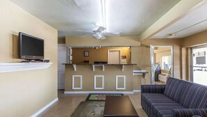 A living room with a sofa, a coffee table, and a television on a stand. There is a kitchen area in the background with a refrigerator and a microwave. - Days Inn by Wyndham Calhoun GA I-75 and US-41 (Calhoun)