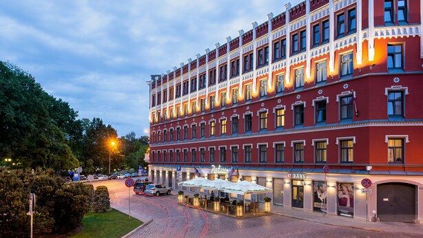 A multi-story hotel with a red facade, multiple windows, and outdoor seating areas. - Radisson Hotel Old Town Riga (Riga)