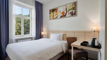 Habitación de hotel con una cama grande, un escritorio con silla, un cuadro en la pared y una ventana con cortinas.