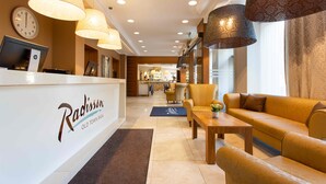 A reception area with a reception desk, a clock, and a seating area with a sofa and chairs. - Radisson Hotel Old Town Riga (Riga)