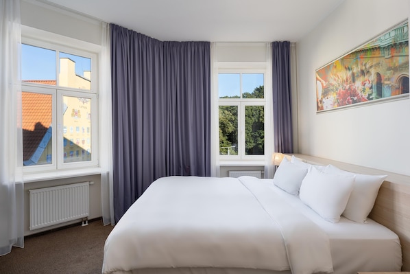 A hotel room with a large bed, two windows with curtains, a radiator, and a painting on the wall. - Radisson Hotel Old Town Riga (Riga)