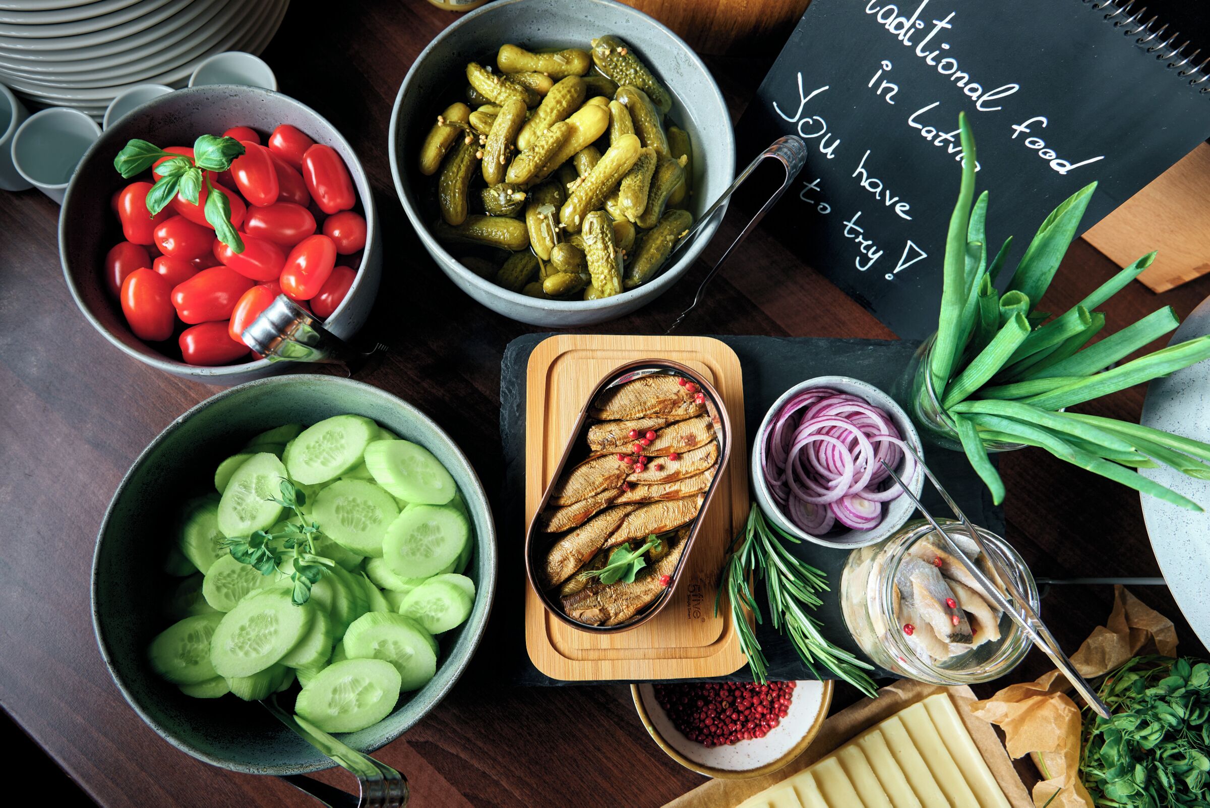 A table with various food items including tomatoes, pickles, cucumbers, and fish.