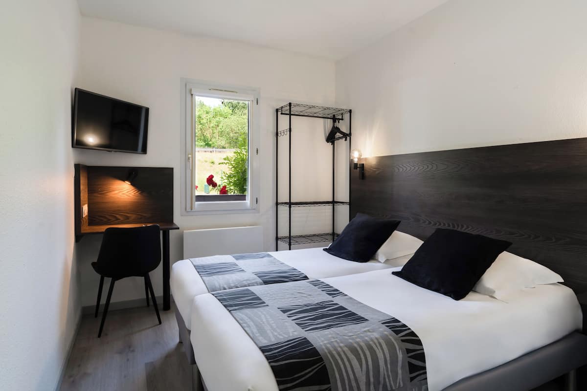 Ein Schlafzimmer mit einem Bett, einem Schreibtisch, einem Stuhl, einem Fernseher, einem Fenster und einer Wandleuchte.