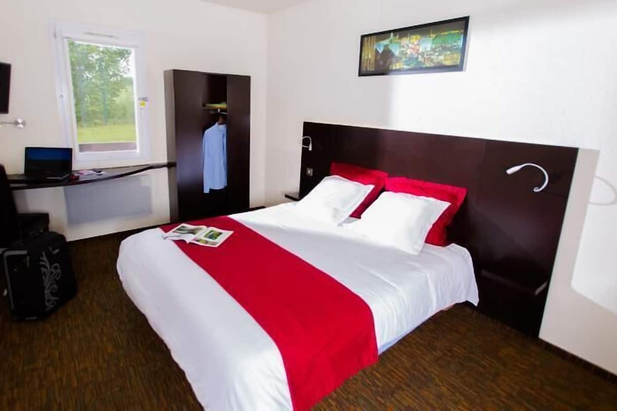 Ein Hotelzimmer mit Bett, Schreibtisch, Stuhl, Fernseher und Fenster.