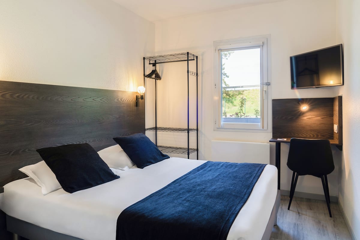 Ein Hotelzimmer mit Bett, Schreibtisch, Stuhl, Fernseher und Fenster.