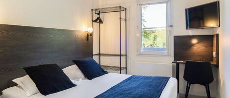A hotel room with a bed, a desk, a chair, a TV, and a window.