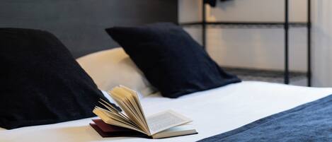 A neatly made bed with a book open on it, a dark blanket, and a pillow.