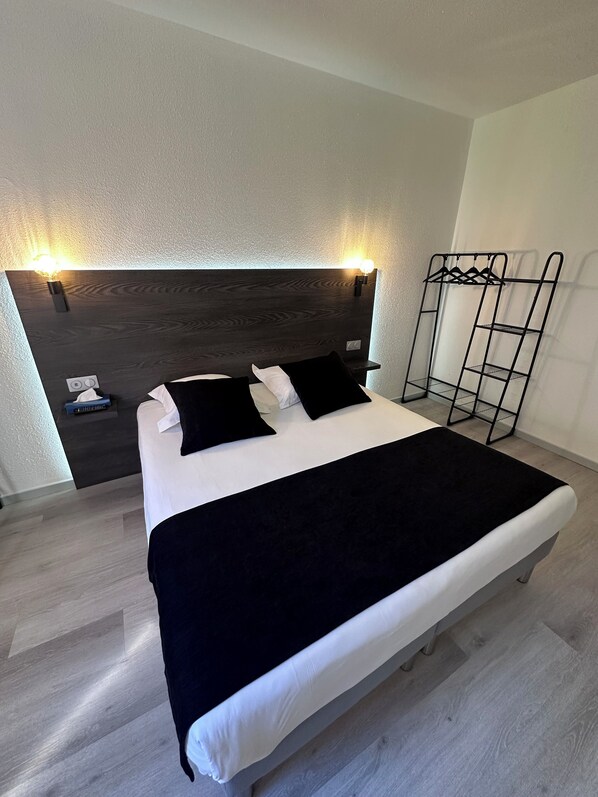 A bed with a dark headboard, a black throw blanket, and two black pillows.