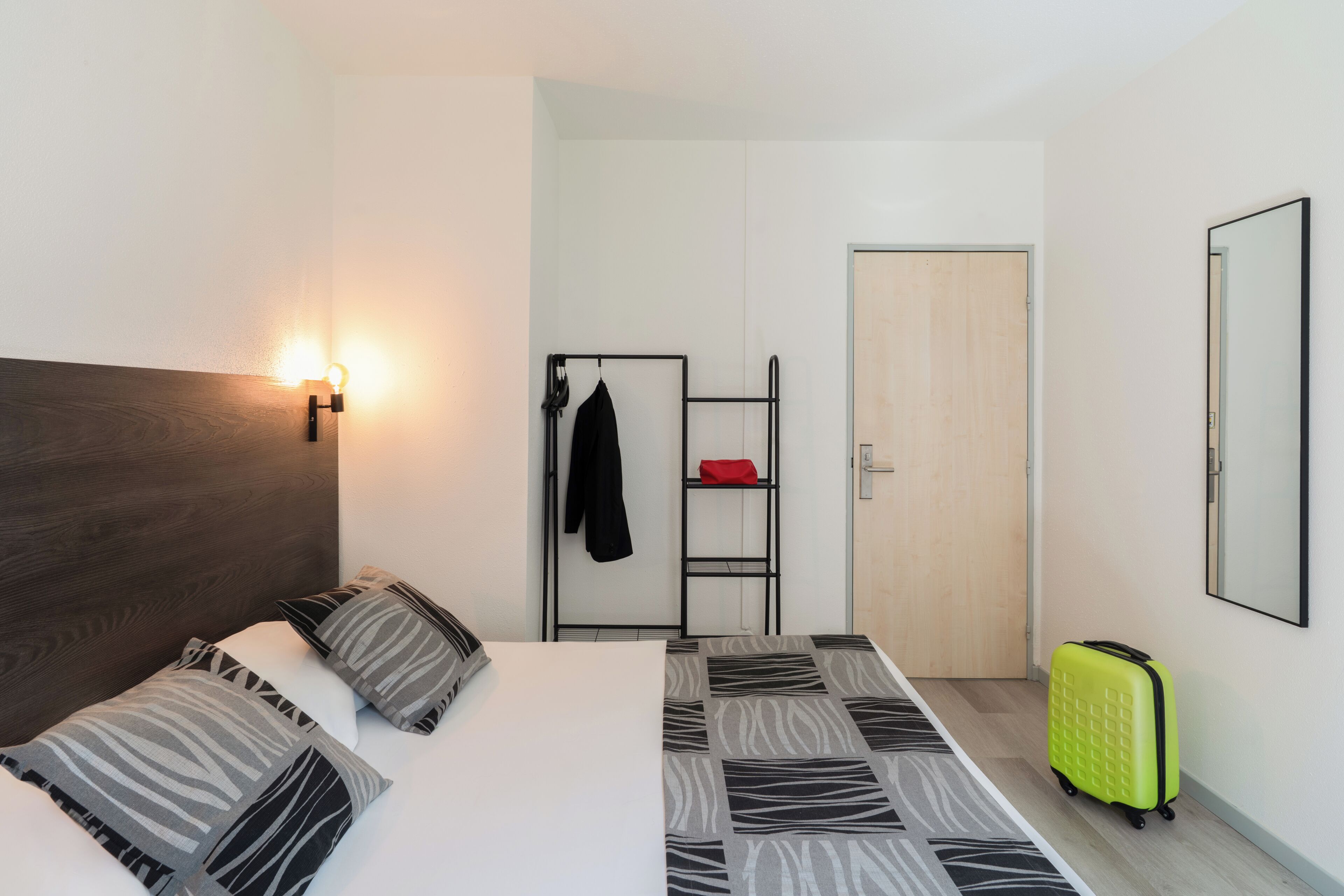 Una habitación de hotel con una cama, un armario, un espejo y una maleta.