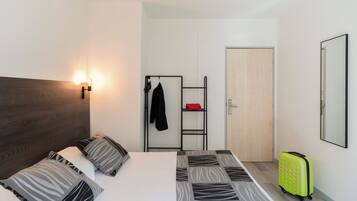 Una habitación de hotel con una cama, un armario, un espejo y una maleta.