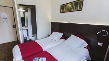 A hotel room with two beds, a shower area, and a wall-mounted artwork.