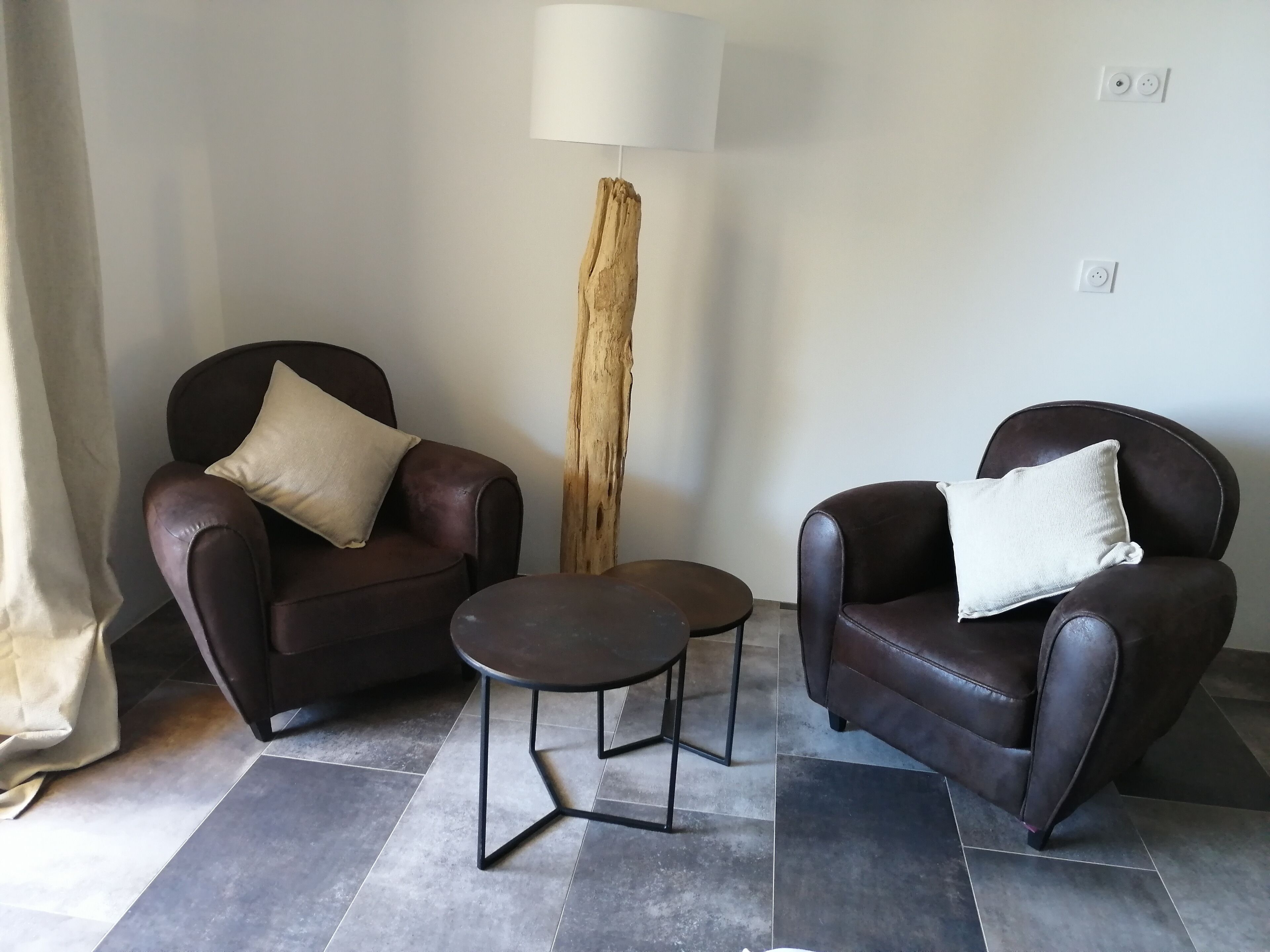 Un salon moderne avec deux fauteuils en cuir, une petite table ronde et une grande sculpture en bois.