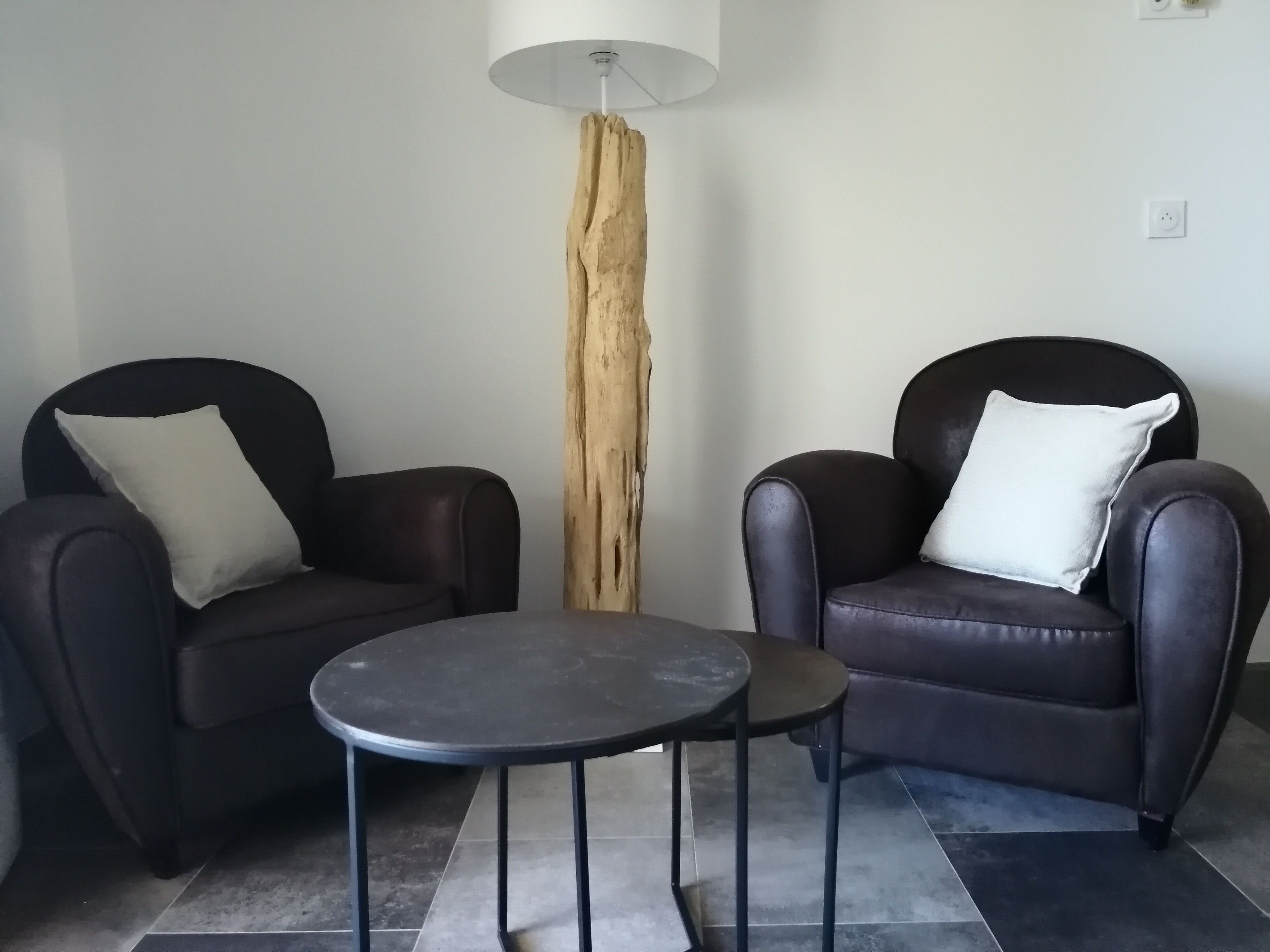 A modern living room with two leather armchairs, a small round table, and a tall wooden floor lamp.