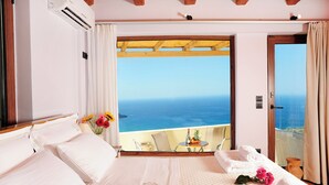 Une chambre avec un grand lit, une vue sur la mer et un balcon équipé d’une table et de chaises.