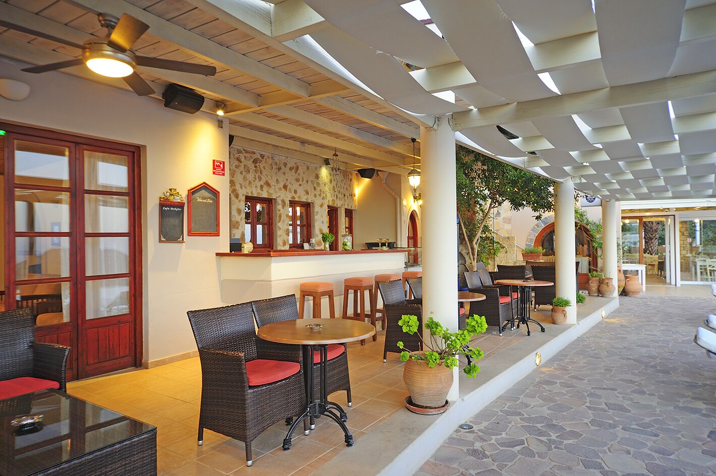 An outdoor cafe area with wicker furniture, a bar counter, and potted plants.