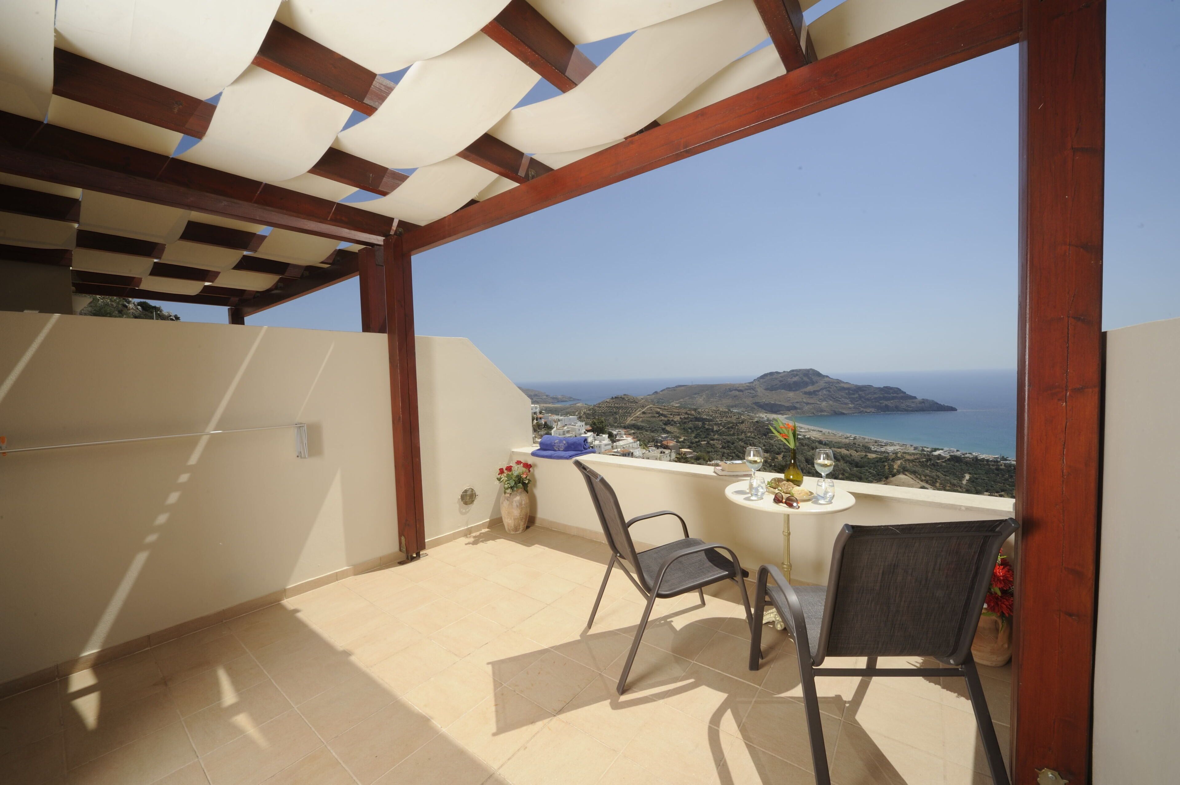 A balcony with a view of the sea, a table with a chair, and a vase with flowers.