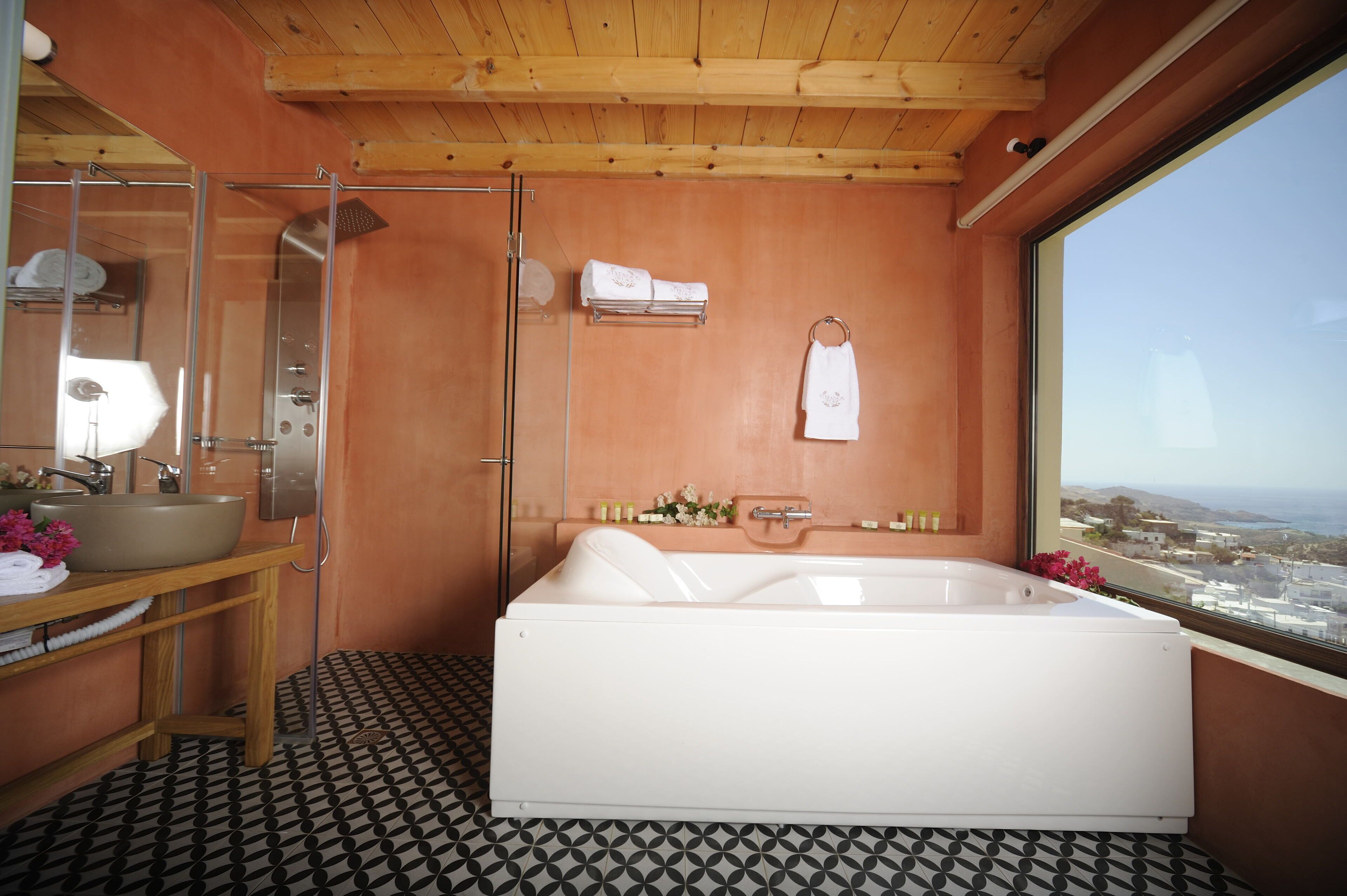 A modern bathroom with a bathtub, a glass shower enclosure, a wooden vanity, and a large window offering a view.