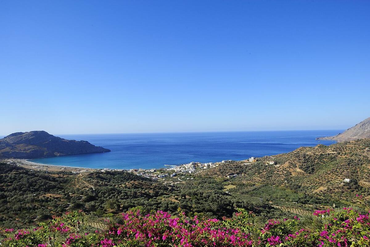 A coastal landscape with a view of the sea, a hill, and a town in the distance.