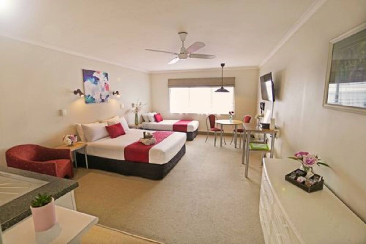 A hotel room with two beds, a desk, a chair, a TV, and a ceiling fan.