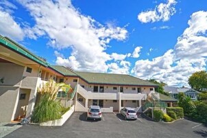 Un motel de dos pisos con estacionamiento, un pasillo cubierto y un techo verde.