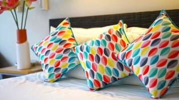 A bed with colorful leaf-patterned pillows and a vase with flowers on a bedside table.
