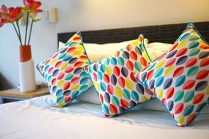 Una cama con almohadas estampadas con hojas y un florero sobre una mesita de noche.