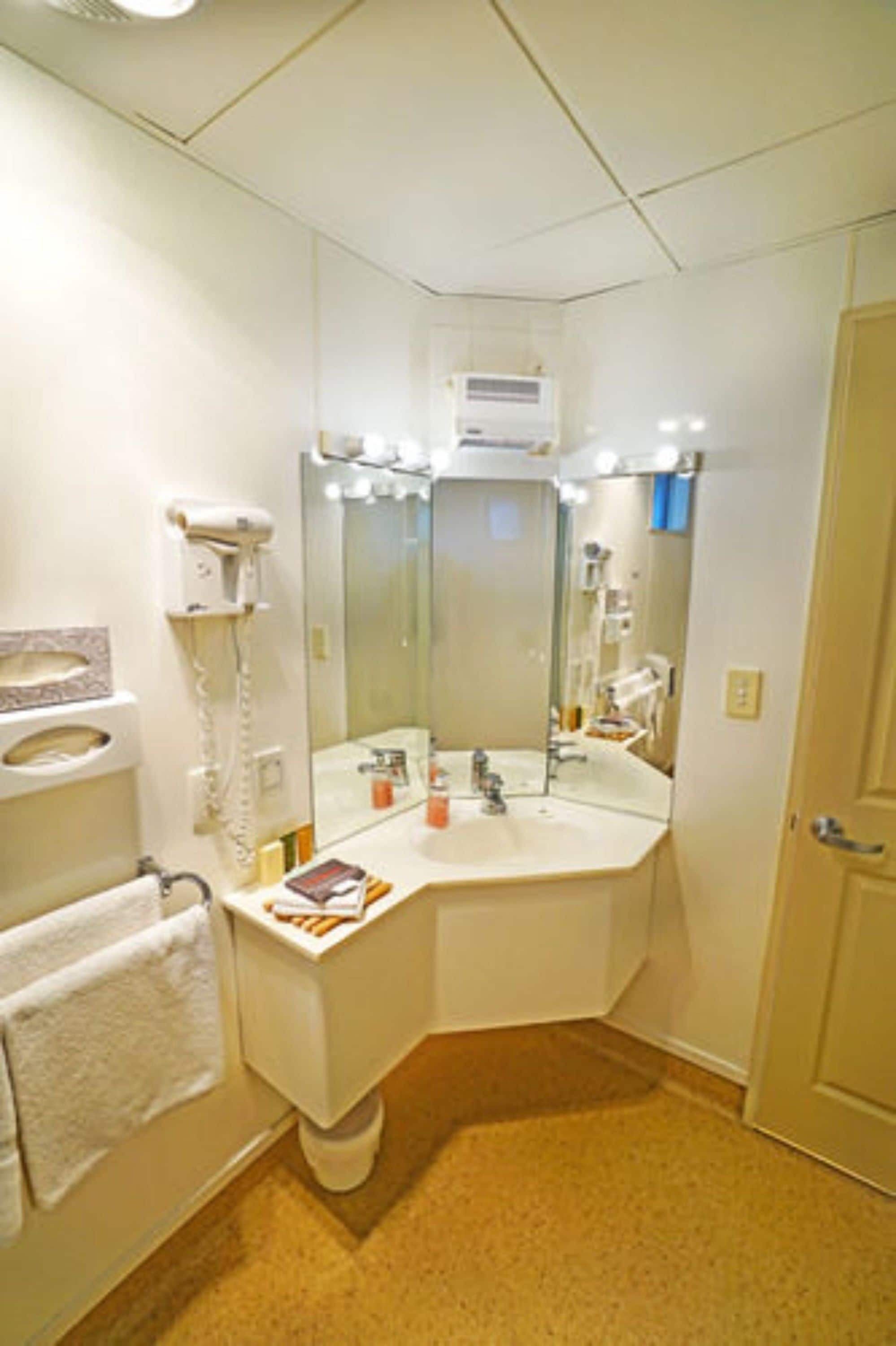 Une salle de bain avec un lavabo blanc, un miroir et un sèche-cheveux fixé au mur.
